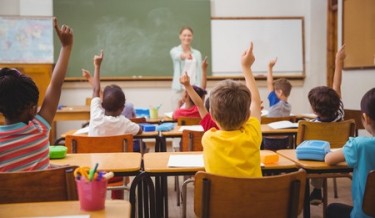 Children in classroom raising hands