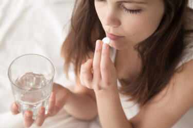 Girl taking white pill and holding glass of water