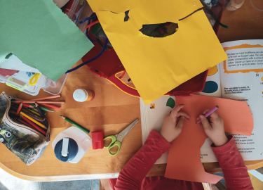 kindergarten work space at school with paper, child's hands, and scissors