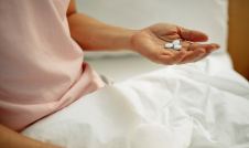 woman sitting on bed holding three white round pills
