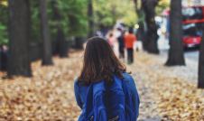 Little girl wearing blue backpack on a sidewalk in an urban area