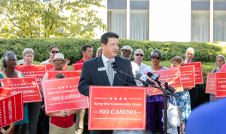 John Rustin speaking at a press conference surrounded by people holding "No Casino" signs