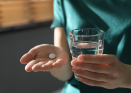 Woman holding white pill and a glass of water